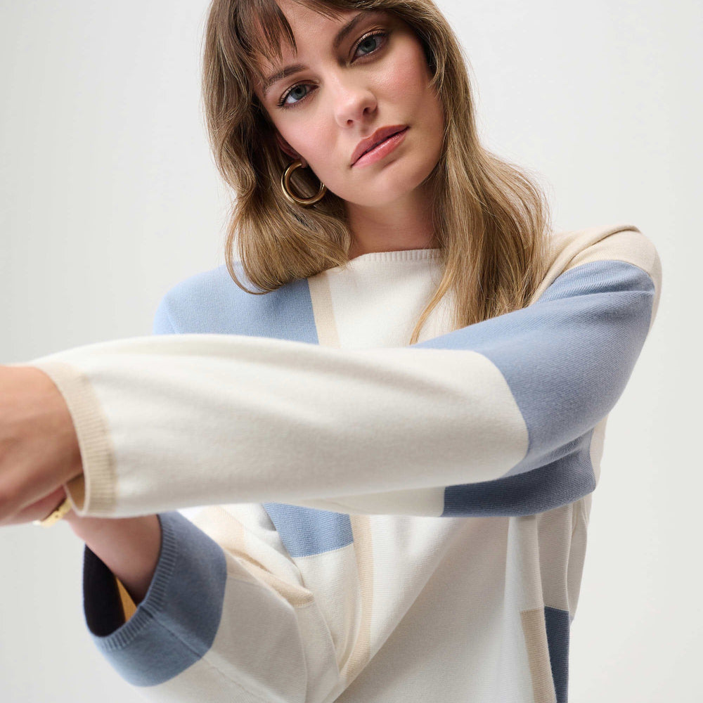 Woman wearing a sweater with a light blue, white and light beige color block design