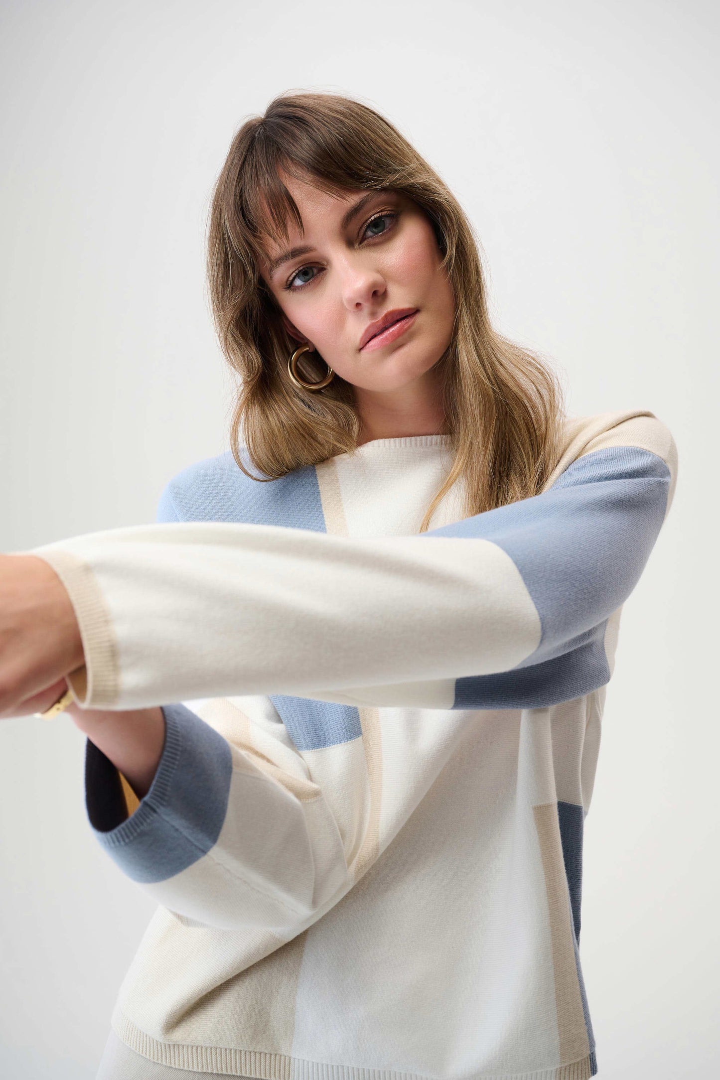 Woman wearing a sweater with a light blue, white and light beige color block design
