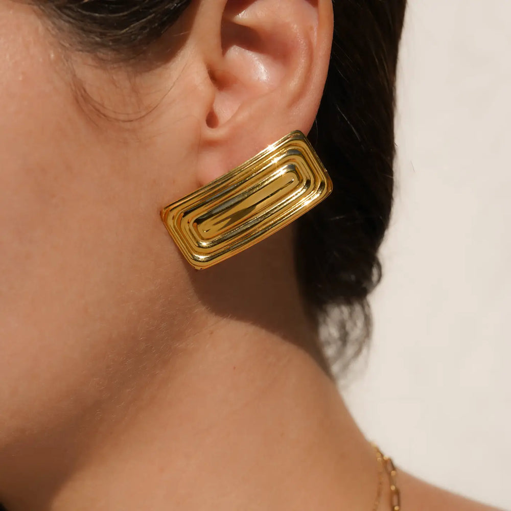 A person wearing gold rectangular earrings