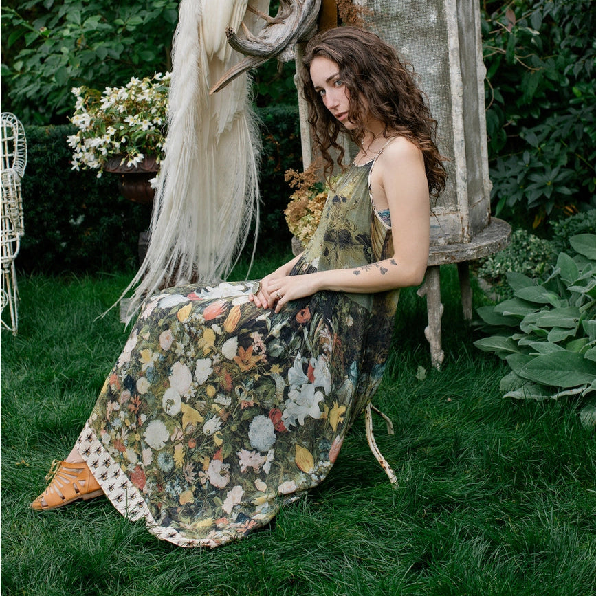 Woman in a floral dress sitting on grass with a peacock in an outdoor setting