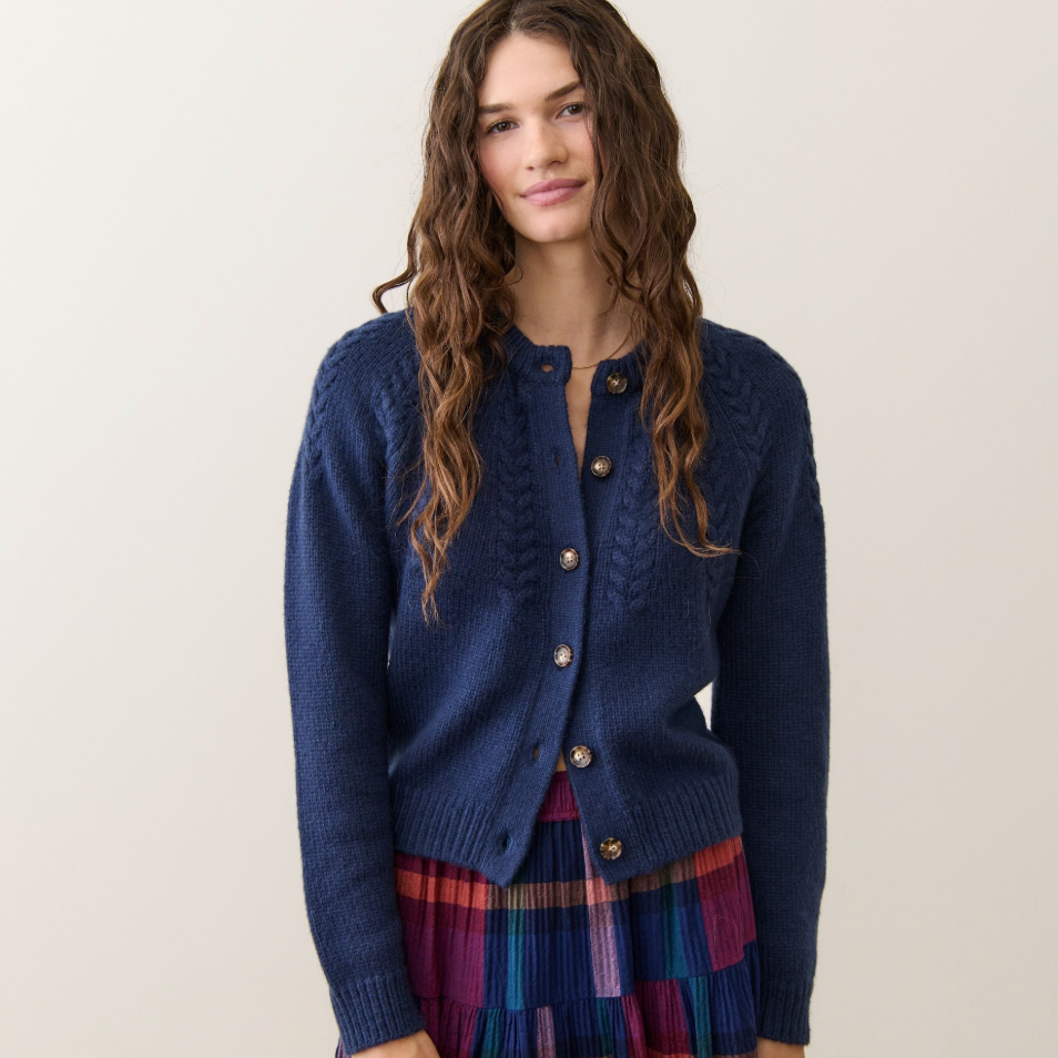 Woman wearing a blue cardigan from Marine Layer over a plaid dress 