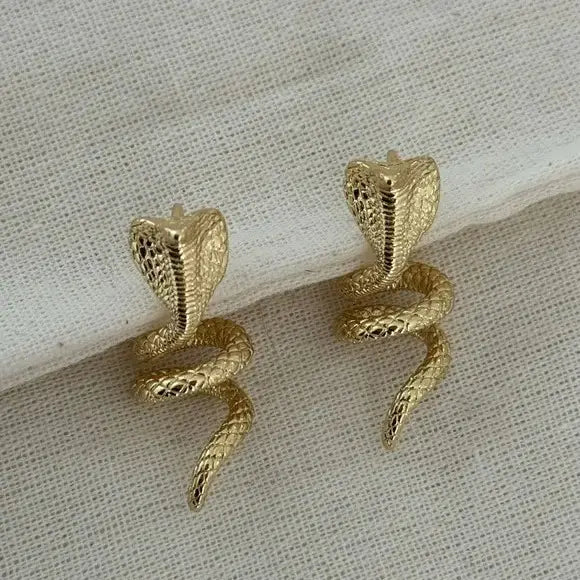 Gold snake-shaped earrings on a textured beige surface