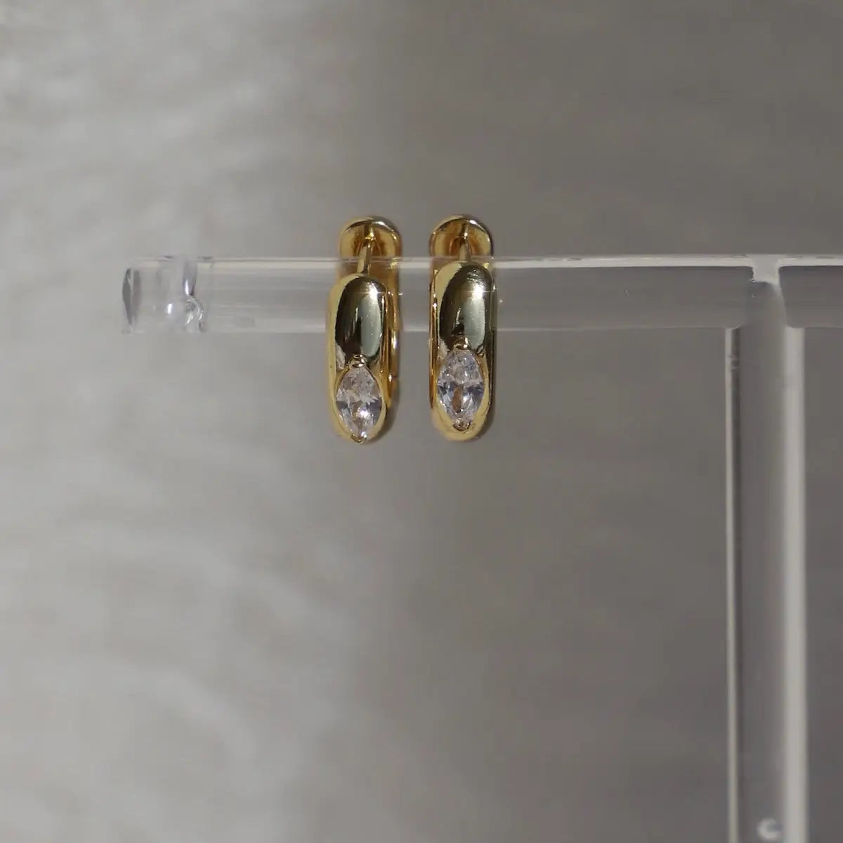 Gold hoop earrings with embedded stones on a clear stand 