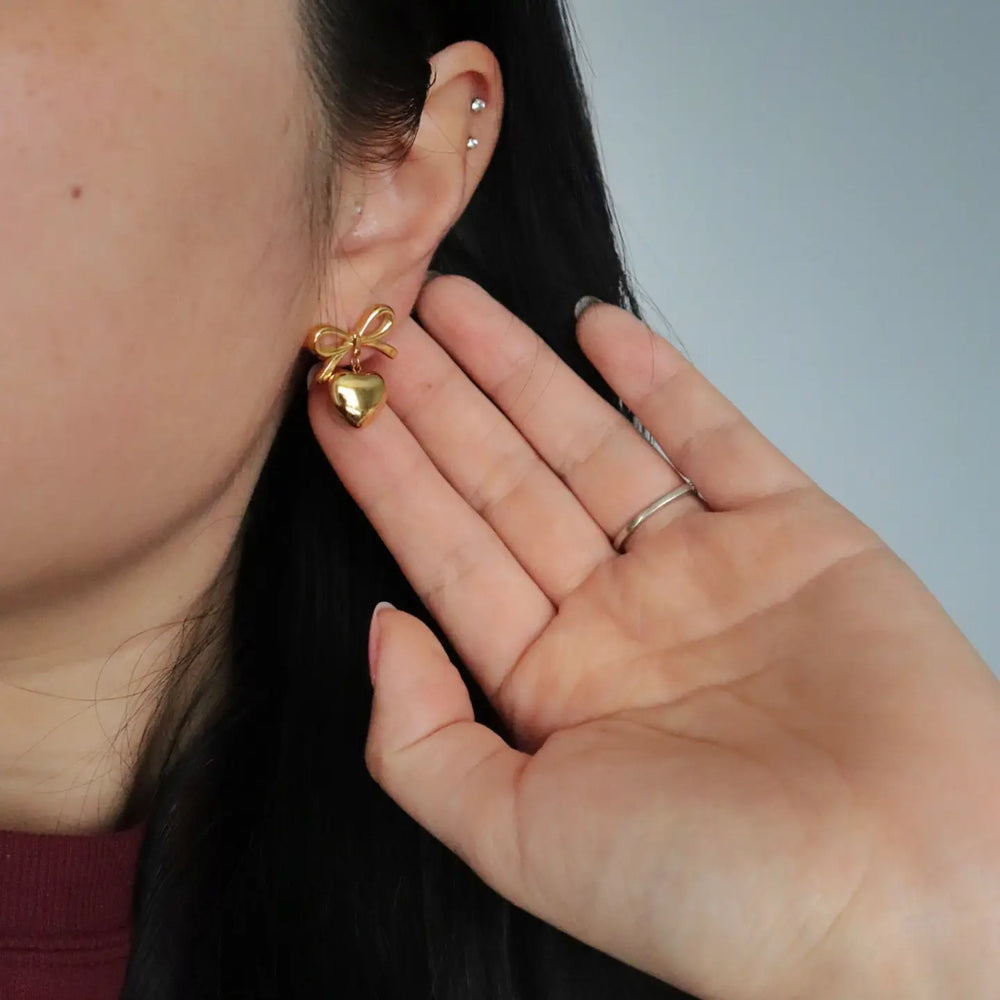 
                      
                        Bow earrings adorned with a small dangling heart
                      
                    