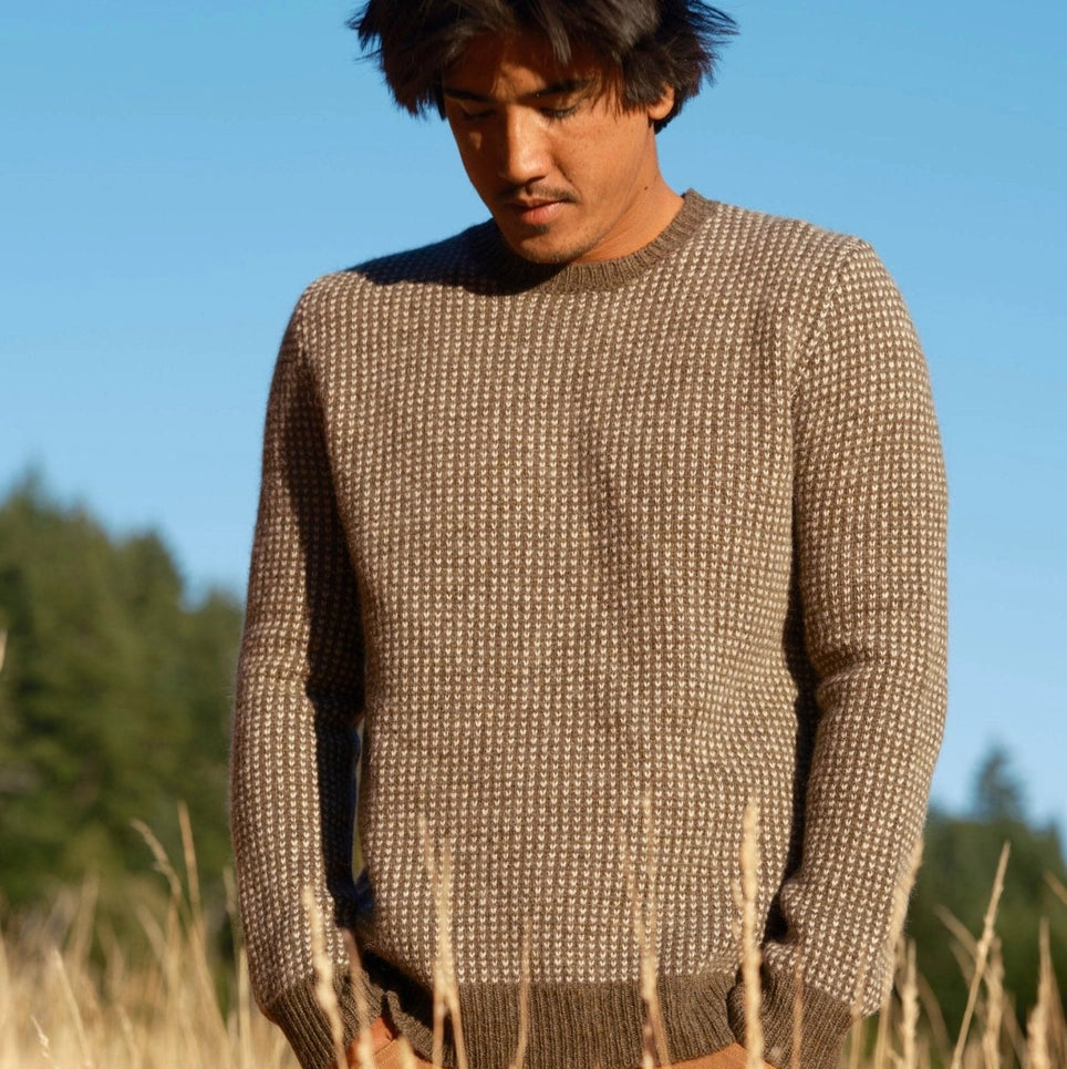 Man wearing a brown knitted sweater from Mollusk while standing in a field with a clear blue sky.