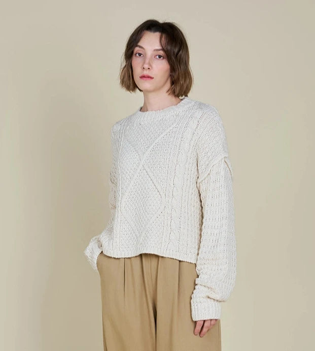 Front view of a woman wearing an ivory cable front crop sweater