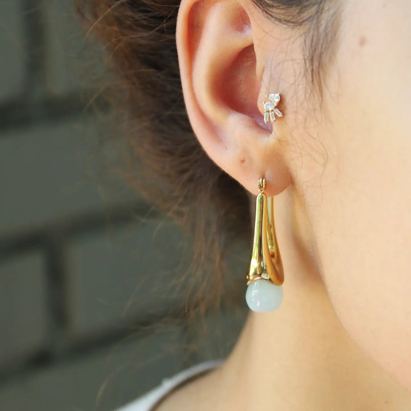 Close-up of an ear wearing a gold earring with a light blue gemstone.