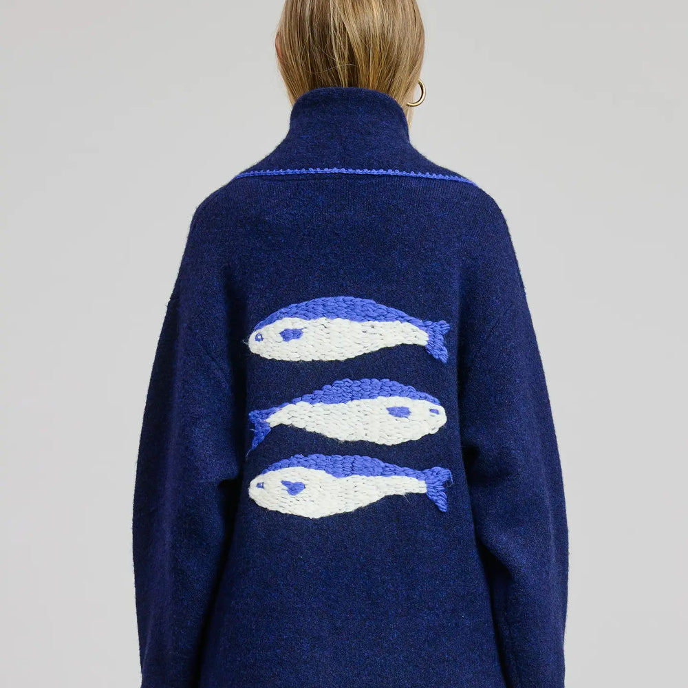 Person wearing a navy blue sweater with fish patterns on the back