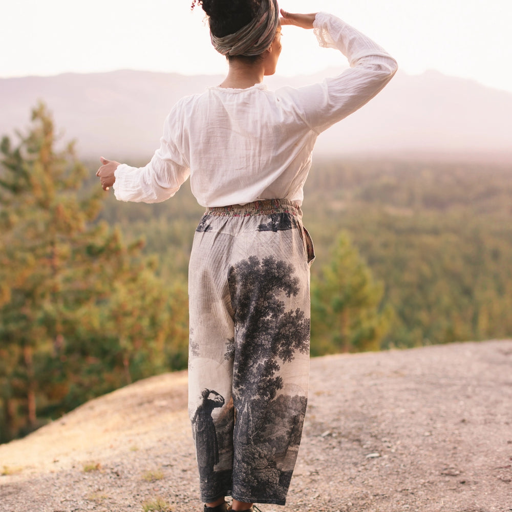 Person standing on a mountain top with hands on head, looking at scenic view