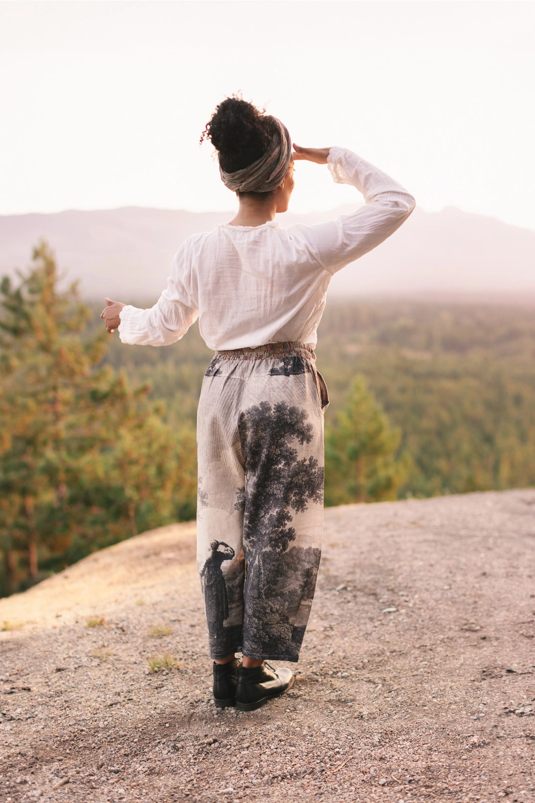 Person standing on a mountain top with hands on head, looking at scenic view