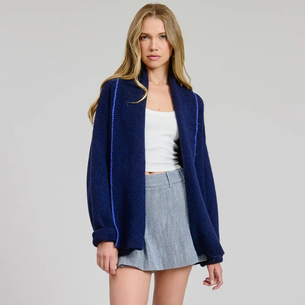 Woman wearing a navy blue cardigan, white top, gray skirt, and white sneakers on a light gray background