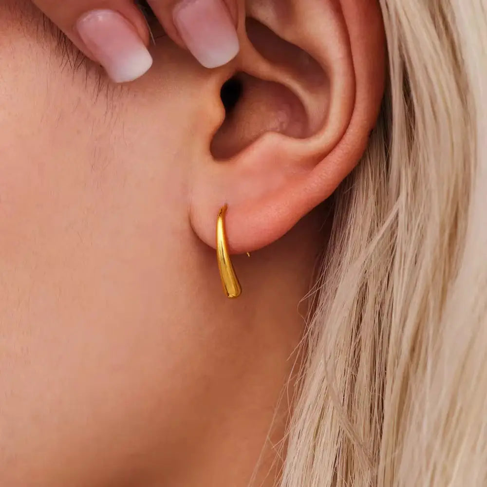Woman wearing earrings with a softly curved drop in high polished gold