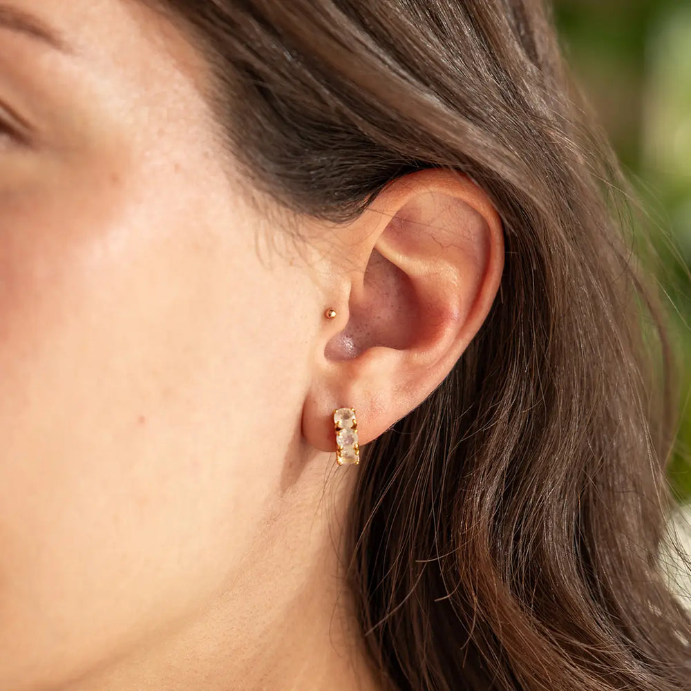 Woman wearing earrings that features a trio of 4mm flashy rainbow moonstones set in a row