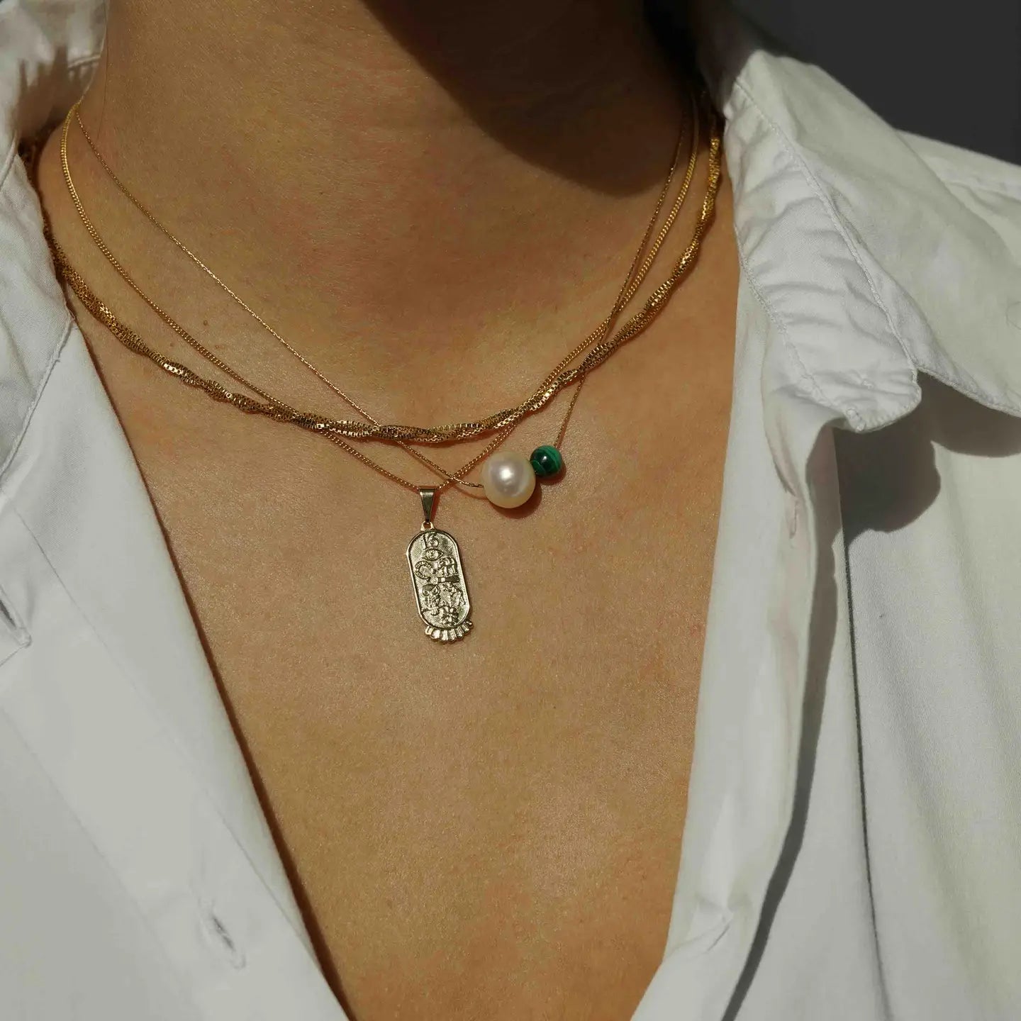 A person wearing the KOZAKH Isla Necklace layered with other chain and pendant necklaces