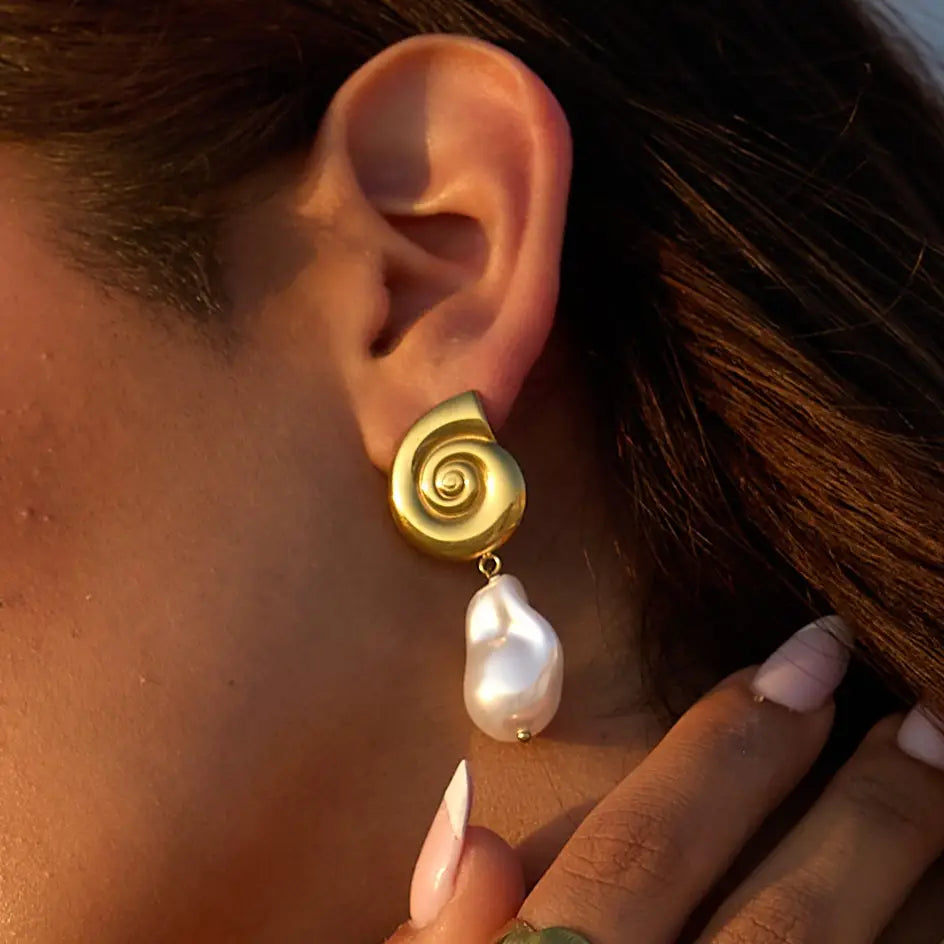 A woman wearing the Liv Bella Vita Oceania Baroque Pearl Conch Earrings