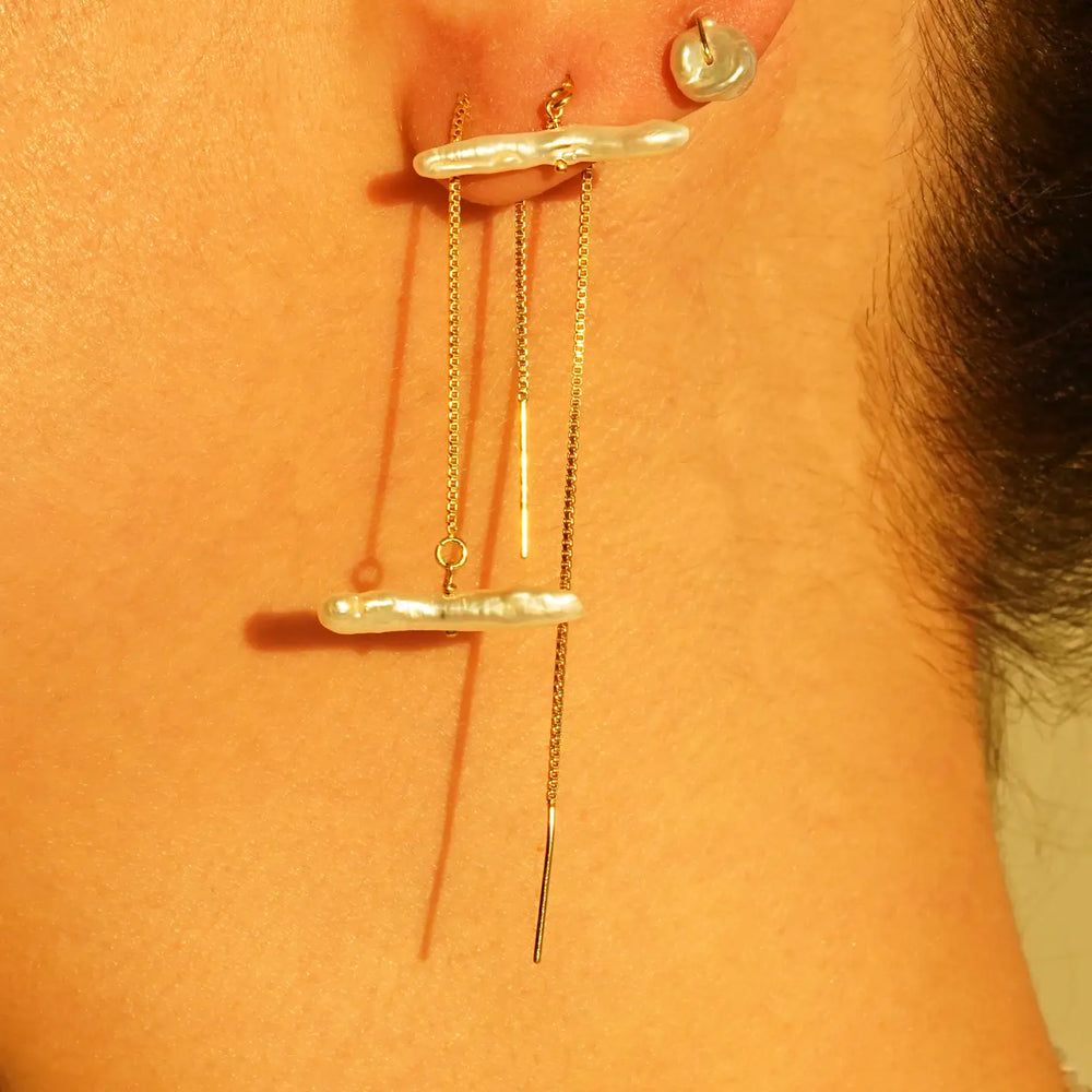 A person wearing gold threader earrings with a freshwater pearl stick
