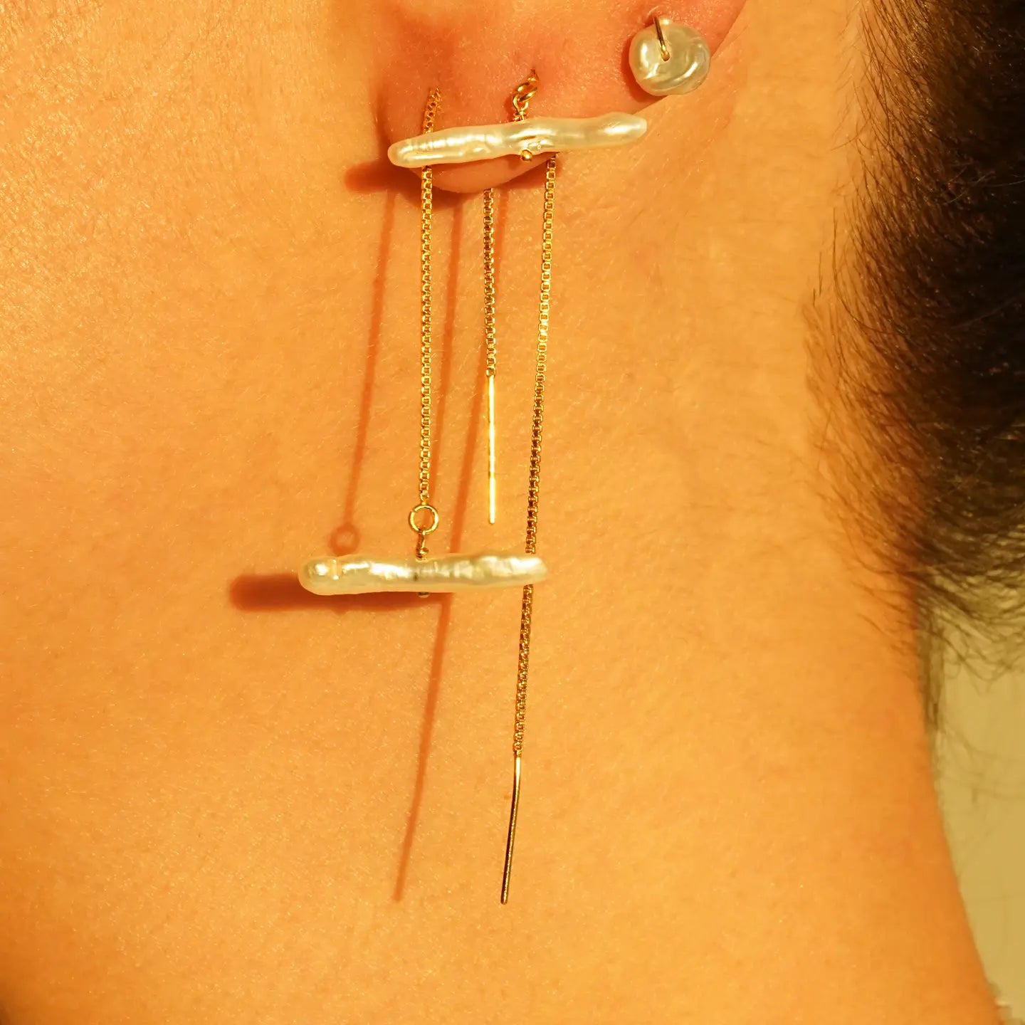 A person wearing gold threader earrings with a freshwater pearl stick