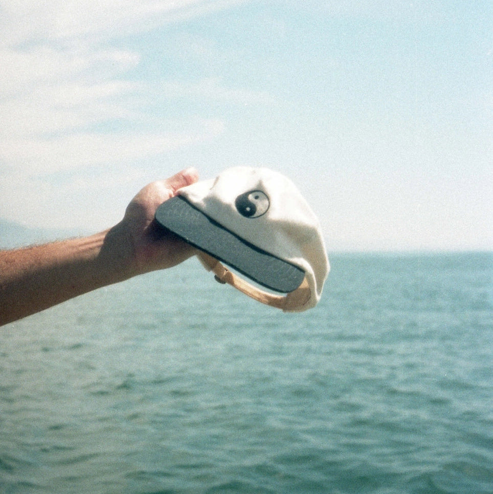 A person holding the Duality Hat by Mollusk over the ocean