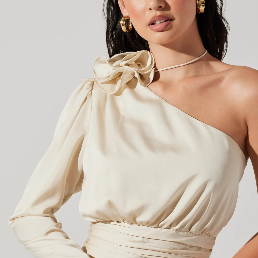 Front view of woman wearing a champagne color satin one shoulder long sleeve top with a corsage detail at the top shoulder