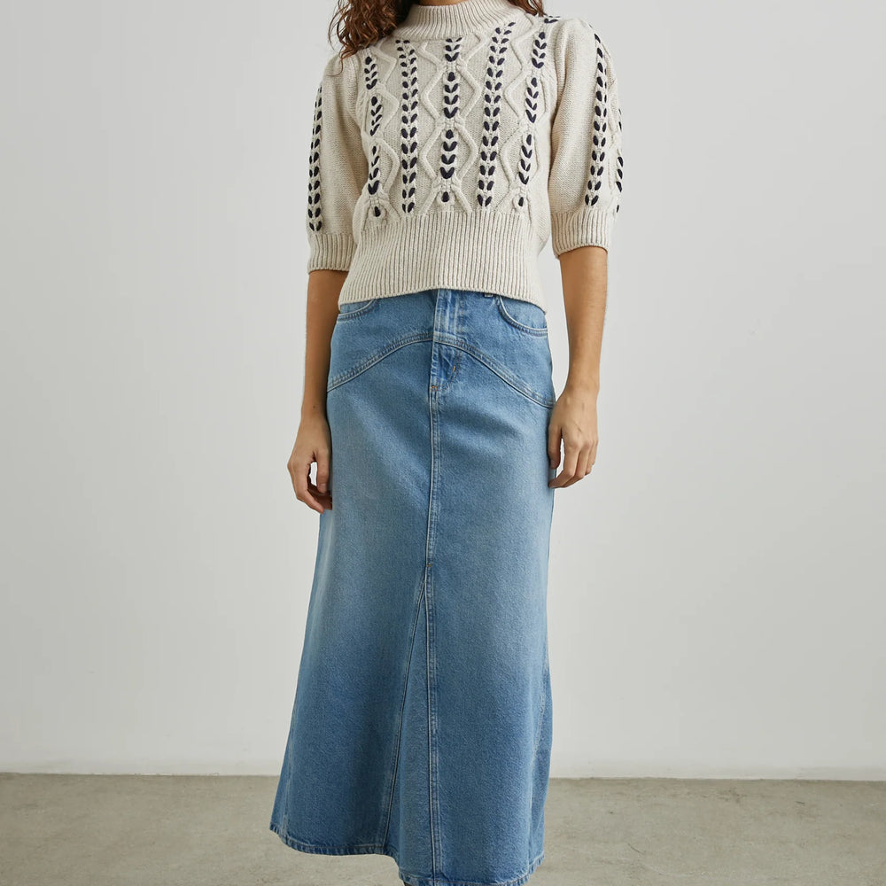 
                      
                        A woman wearing the Addy Cable Knit Sweater by Rails styled with a denim maxi skirt and black boots
                      
                    