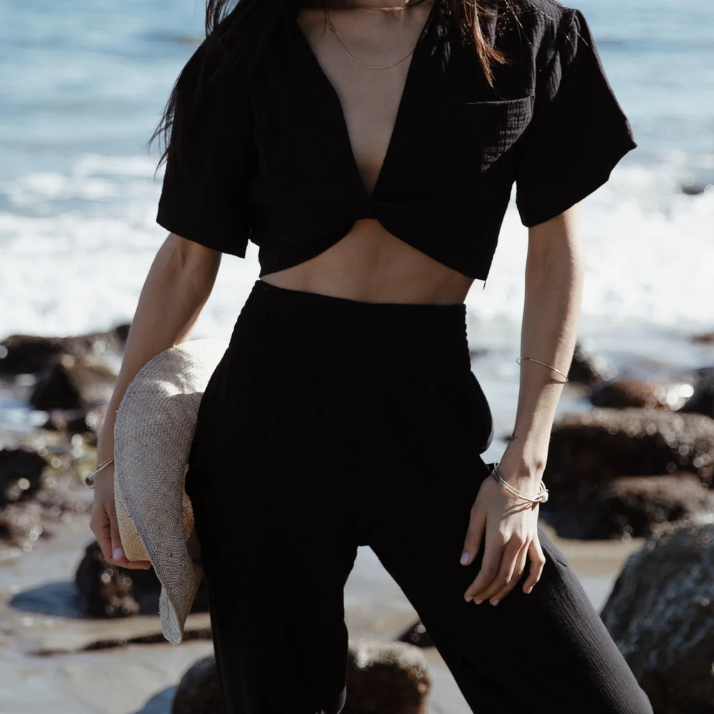 
                      
                        Woman at the beach wearing Stillwater's Knot Front Short Sleeve Shirt in the color Black
                      
                    