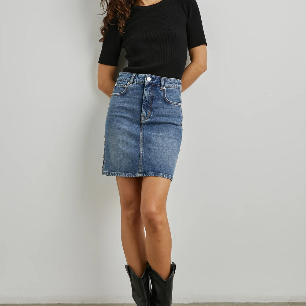 
                      
                        Front view of a woman wearing the denim Starry Night Burbank Mini Skirt from the brand Rails paired with a black top and black boots
                      
                    