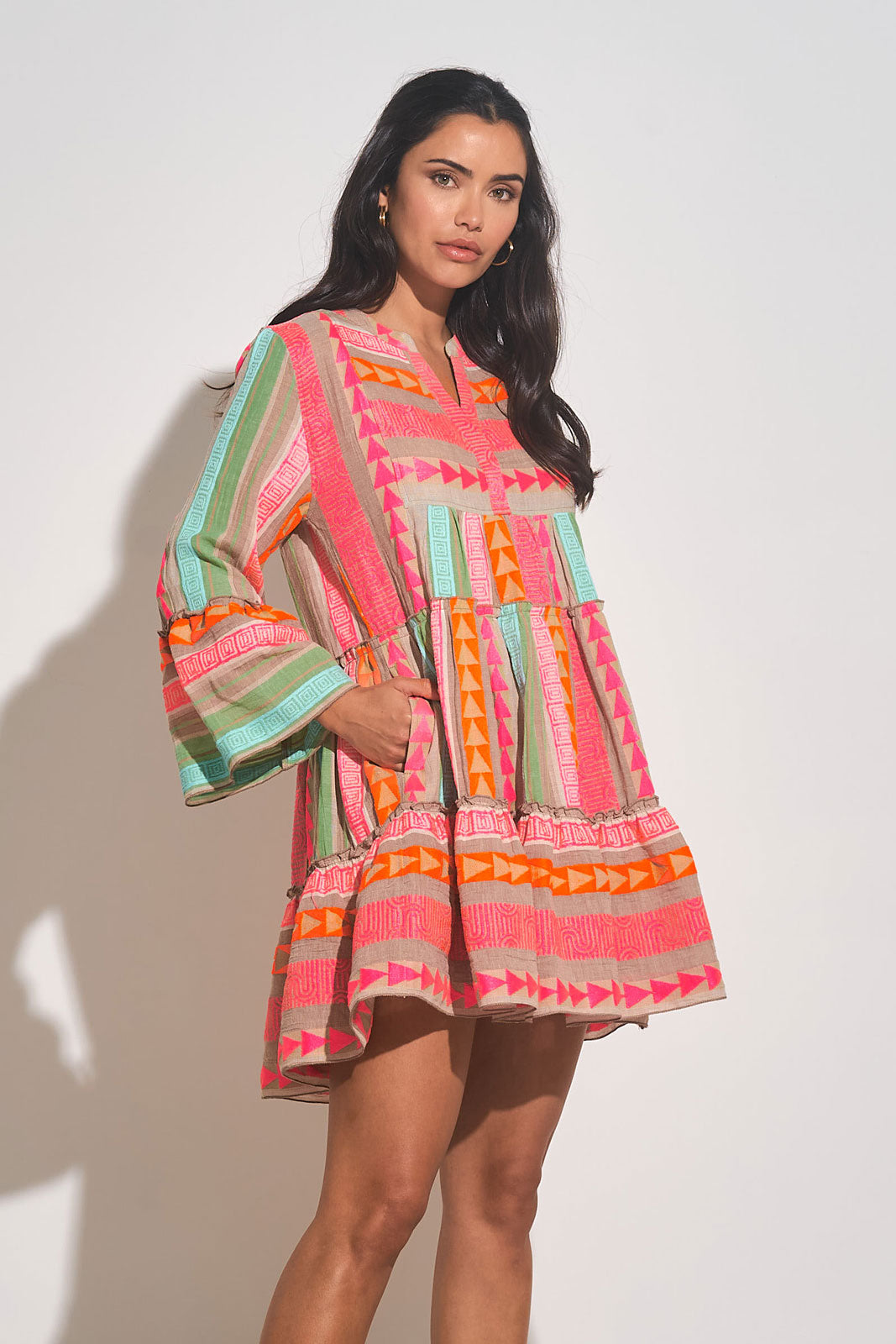 Front side view of woman wearing a multi color mini dress with a a babydoll silhouette and pockets