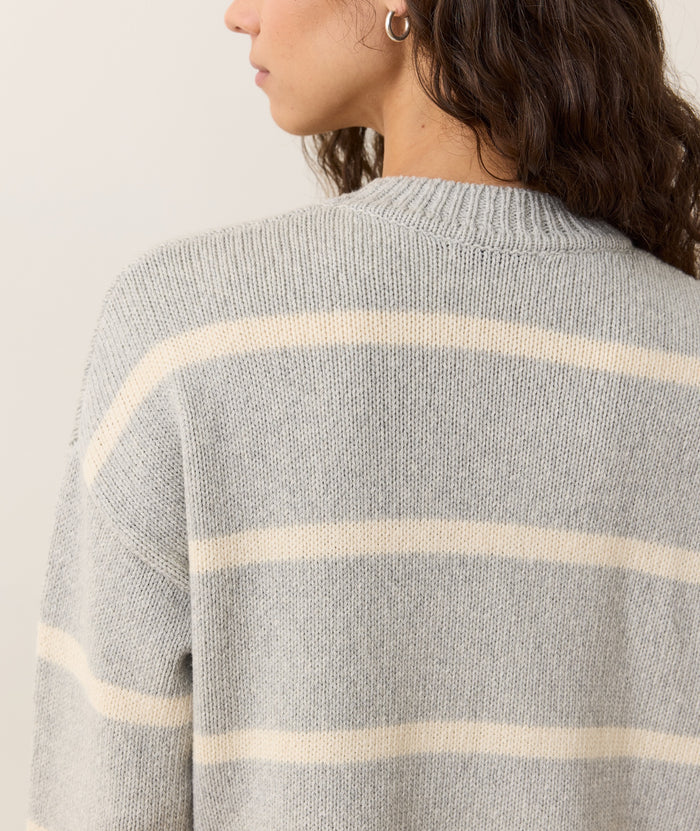 Gray sweater with white stripes worn by a person on a plain background