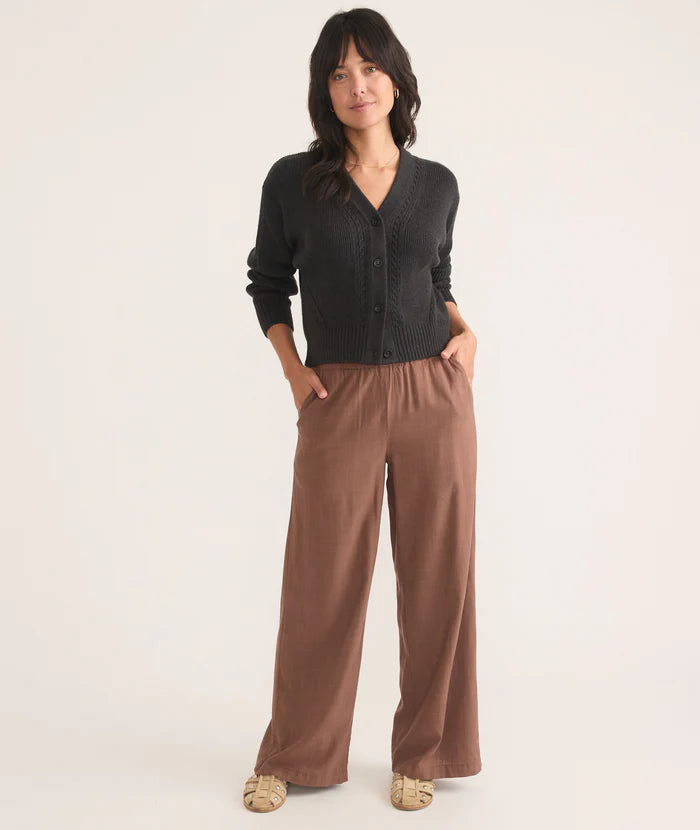 A woman wearing the brown Allison Trousers by Marine Layer. These women's pants have side pockets are paired here with a black cardigan.