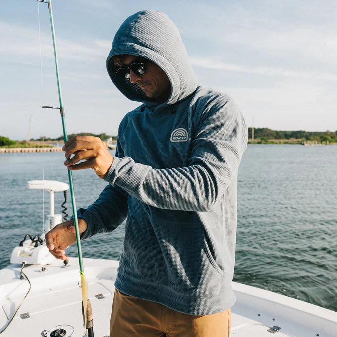 
                      
                        A man fishing while wearing the Mirage Blue Palo Duro Fleece Hoodie by Howler Brothers
                      
                    