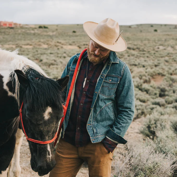 A man standing with a horse while wearing the Petty Mid Wash Denim Depot Jacket by Howler Brothers