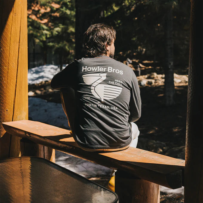 A man sitting in nature while wearing the Pelican Postage Long Sleeve T-Shirt by Howler Brothers