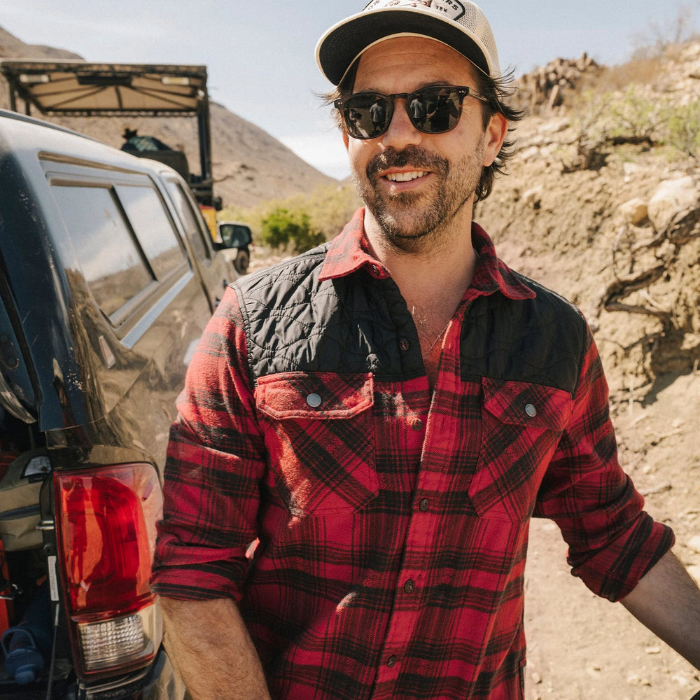 Man in a red plaid shirt with a black quilted yoke, standing outside next to a vehicle