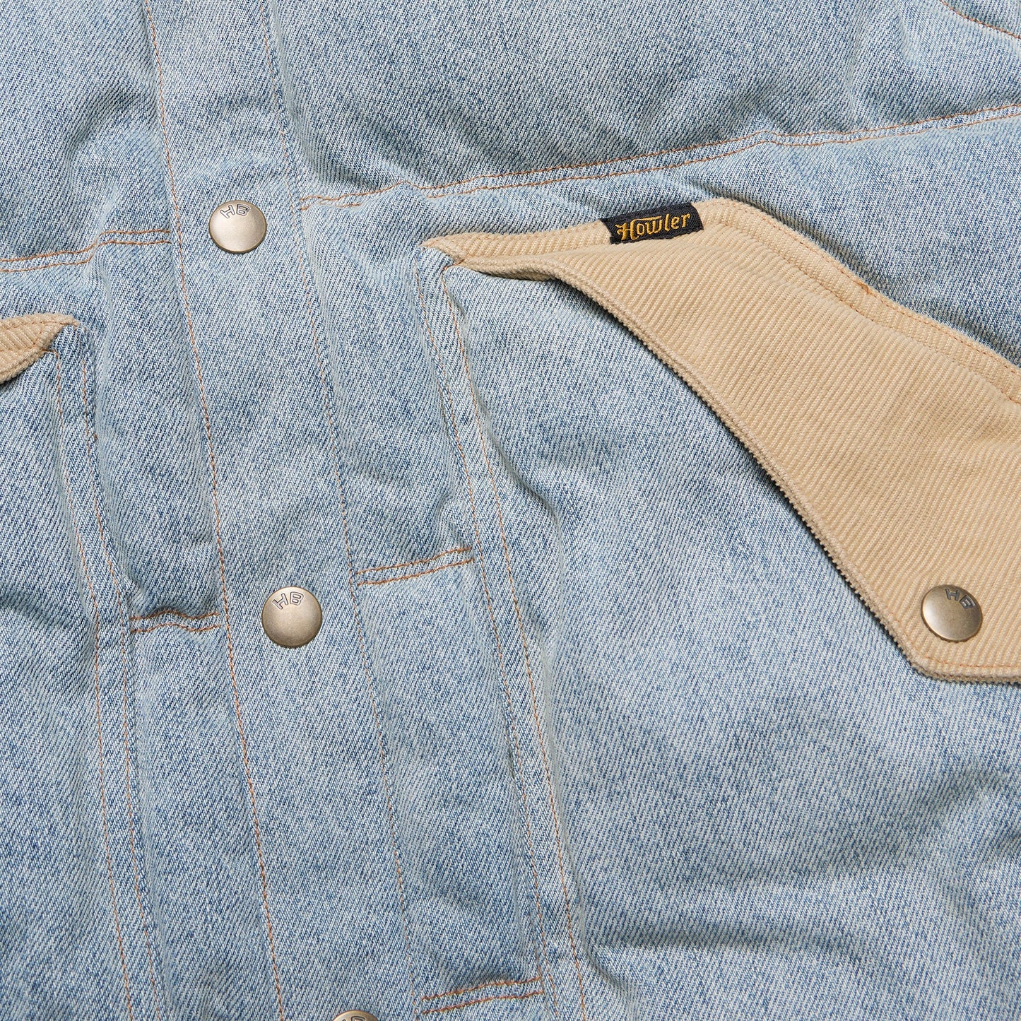Close-up of a denim jacket with beige accents and a Howler label.