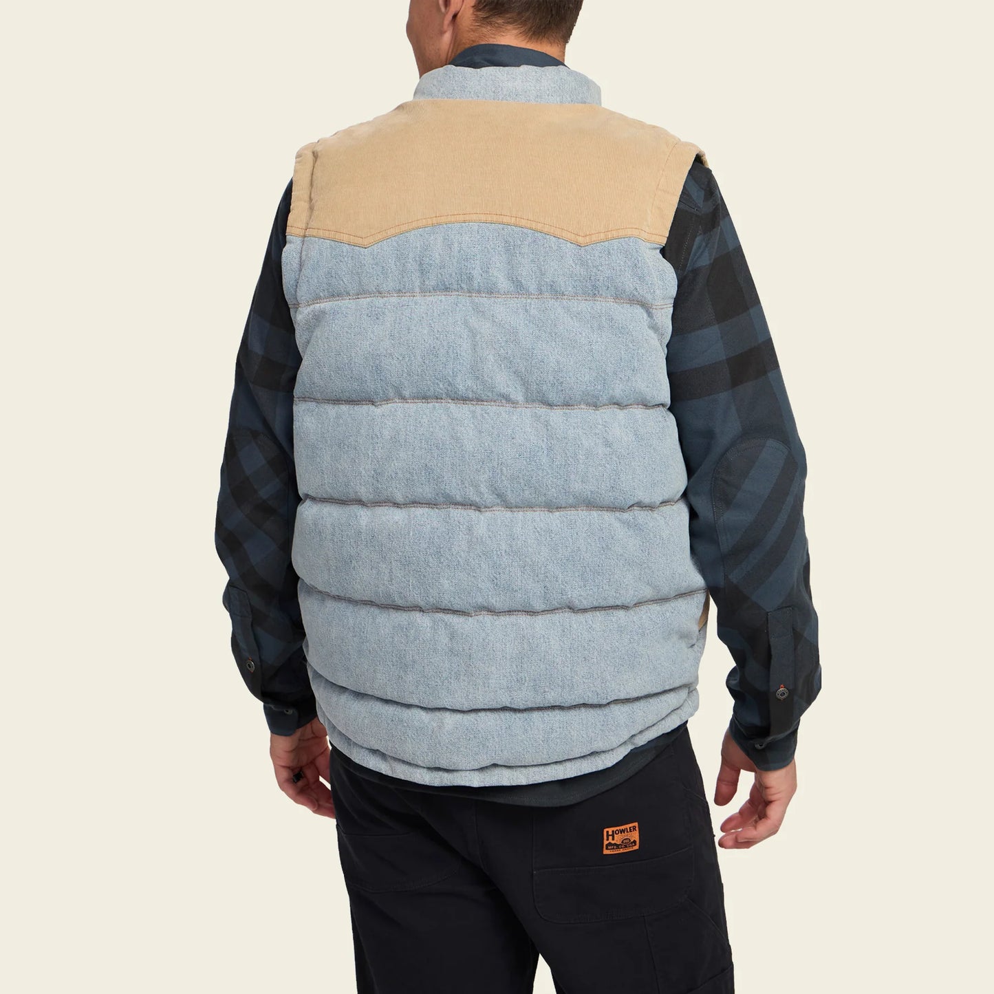 A man wearing a two-tone denim puffer vest with beige and blue sections 