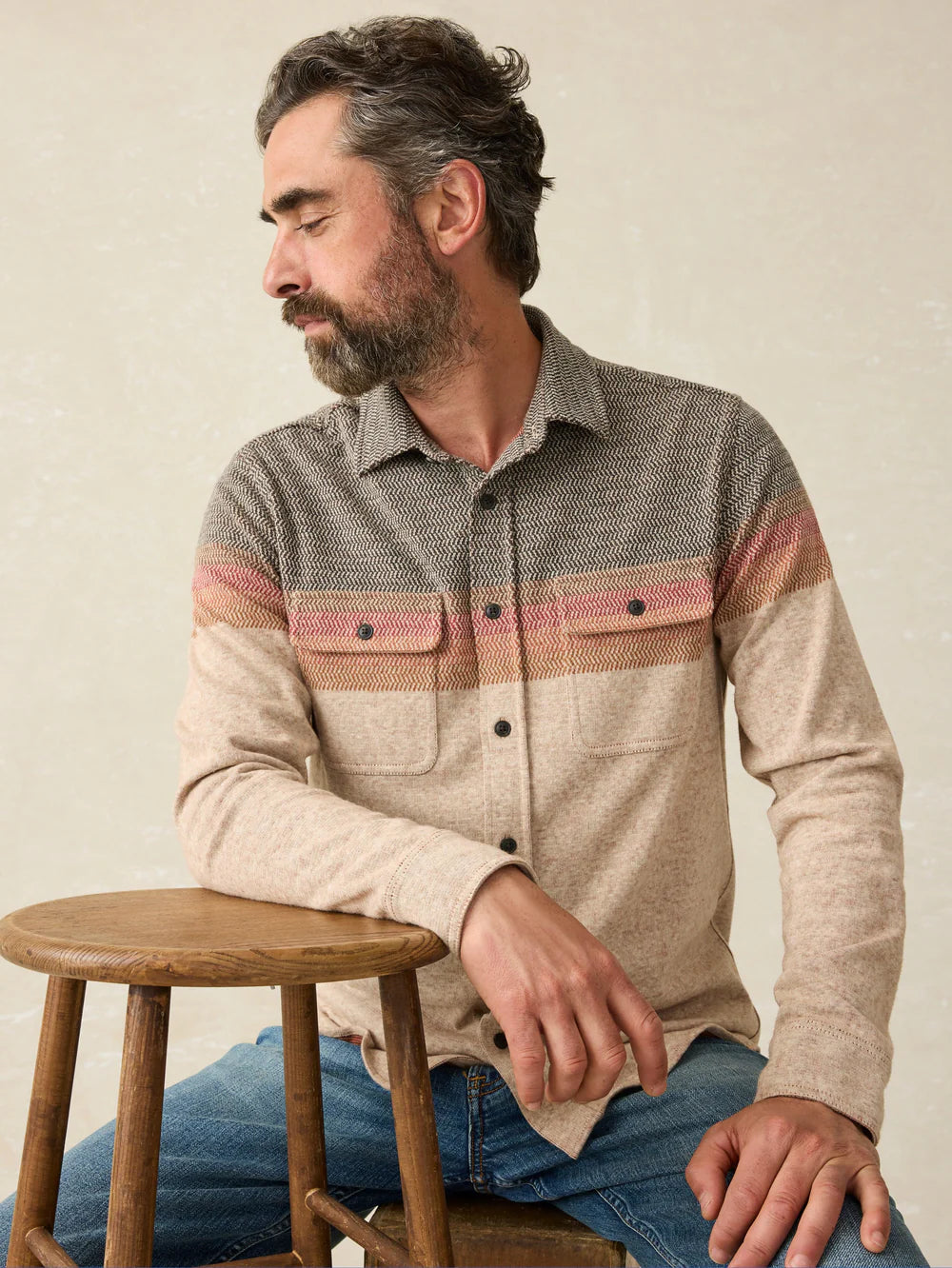 A man sitting by a stool while wearing the Autumn Coast Legend Sweater Shirt by Faherty