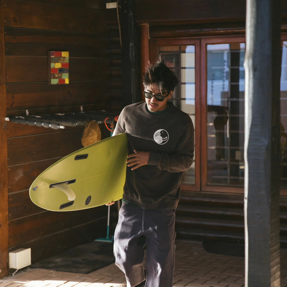 
                      
                        lifestyle photo showing man carrying surfboard while wearing the Surf Society Crew by Mollusk
                      
                    