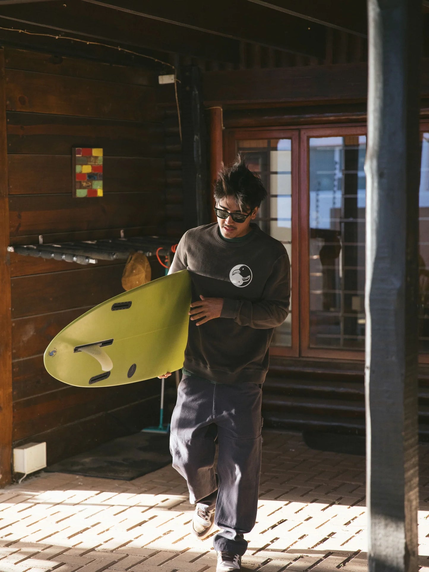 lifestyle photo showing man carrying surfboard while wearing the Surf Society Crew by Mollusk