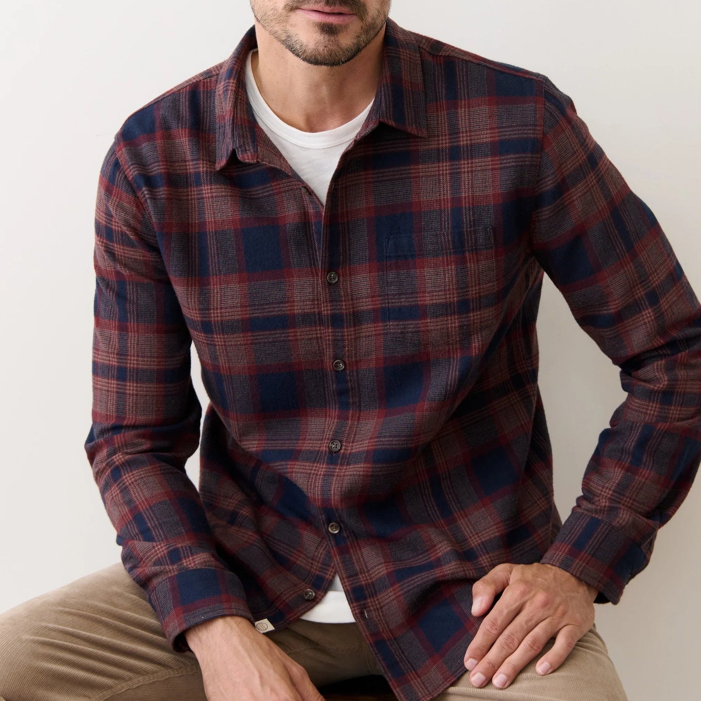 Man wearing a plaid shirt sitting on a stool against a plain background