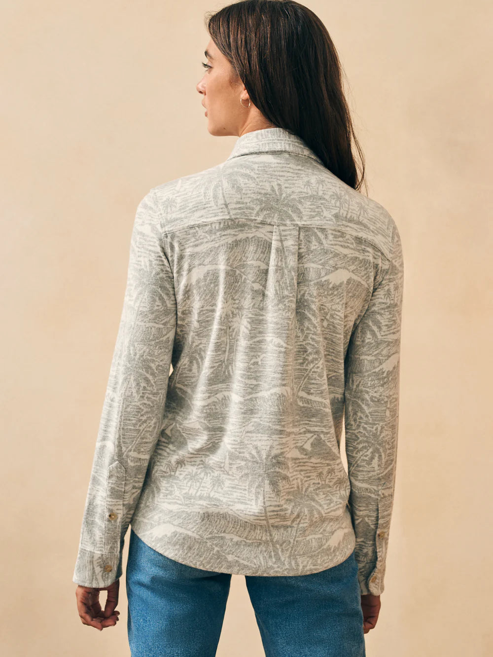 Back view of woman wearing a long sleeve button up shirt with an understated palm tree and wave print throughout