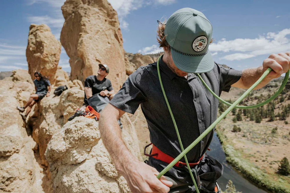 
                      
                        A man wearing the Tundra Hybro Strapback Hat by Roark while rock climbing
                      
                    