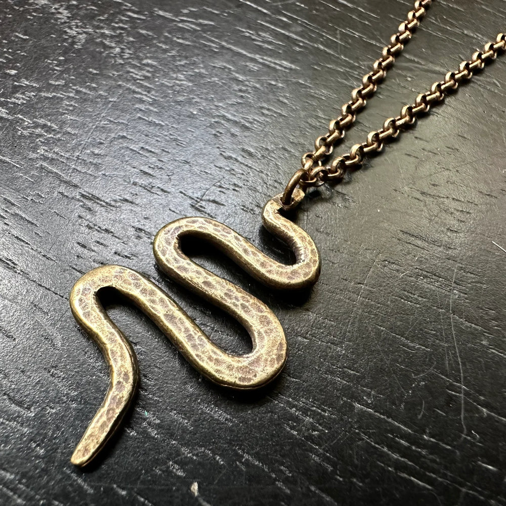 Brass snake-shaped pendant on a a brass chain against a dark textured background