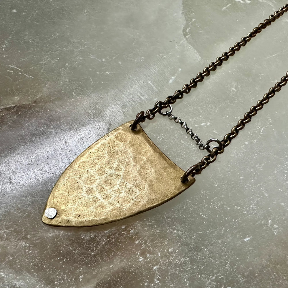 Necklace with a large, textured  spear pendant on a gray surface