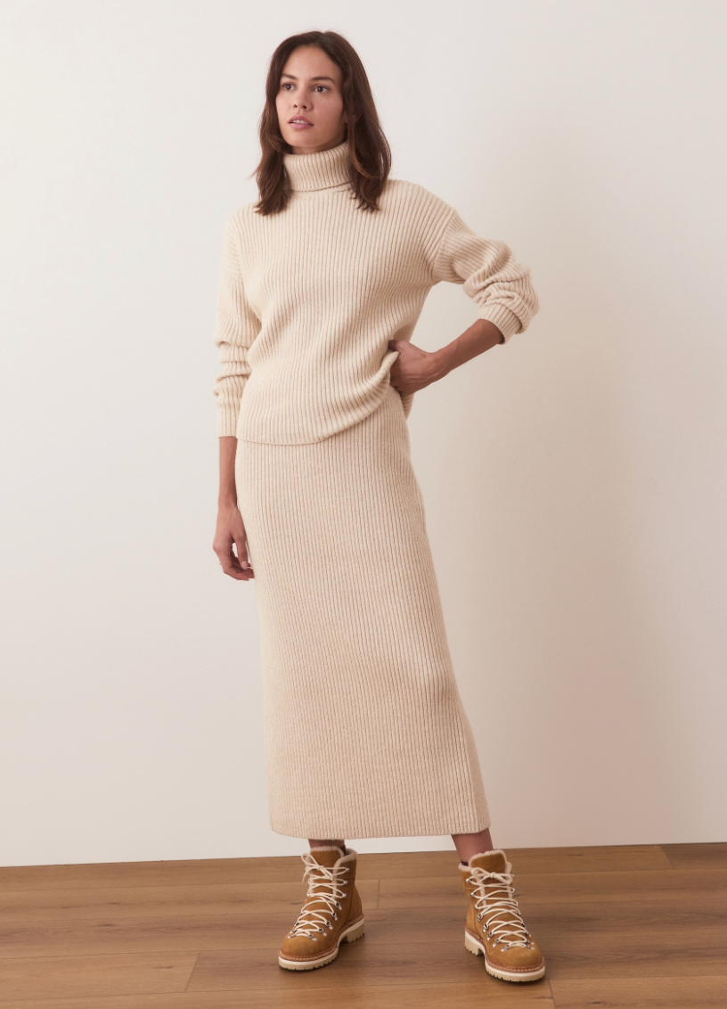 A woman wearing the Isla Knit Turtleneck by Marine Layer in the color Cream paired with a matching skirt