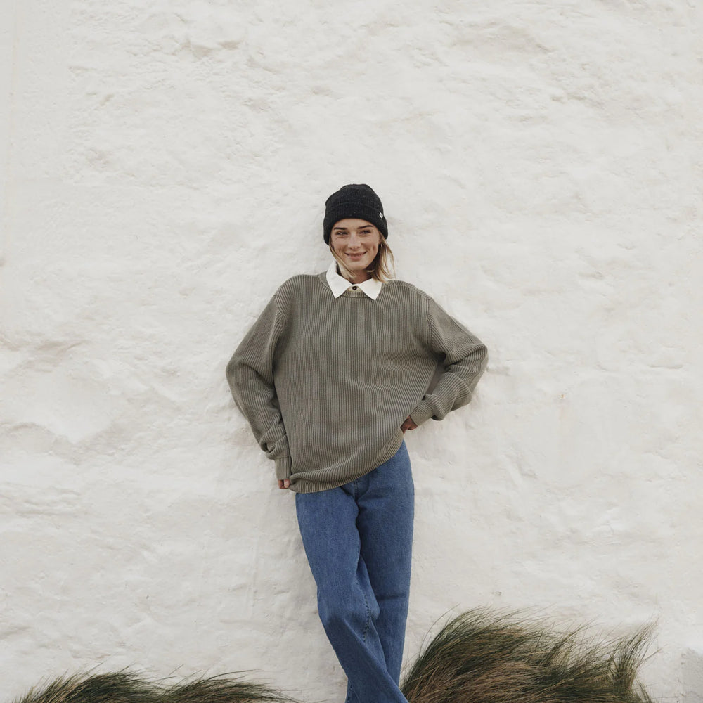 
                      
                        Woman wearing the Moss Swell Sweater by Katin paired with blue jeans standing against a white textured wall with grass at the bottom.
                      
                    