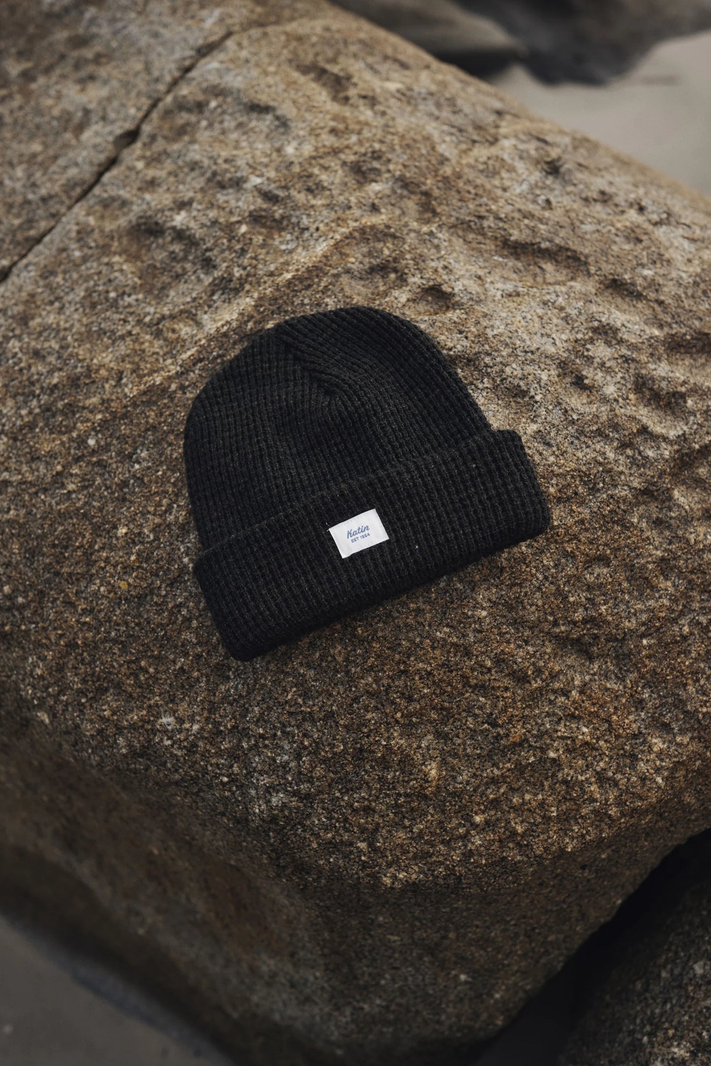 The Black Heather Wade Beanie by Katin on a large rock