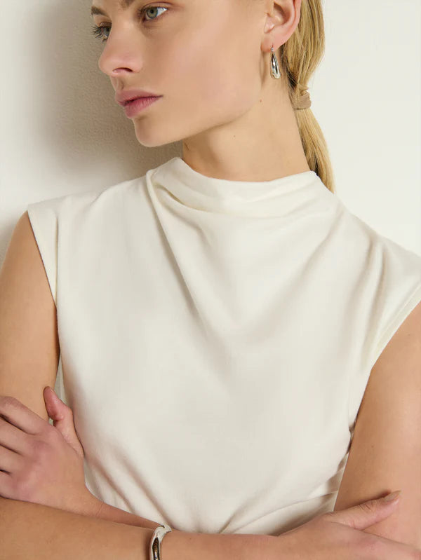 A woman wearing a white sleeveless top with a draping mock neckline