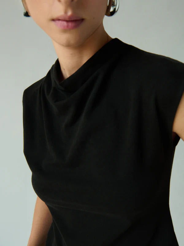 
                      
                        A woman wearing a black sleeveless top with a draping mock neckline
                      
                    