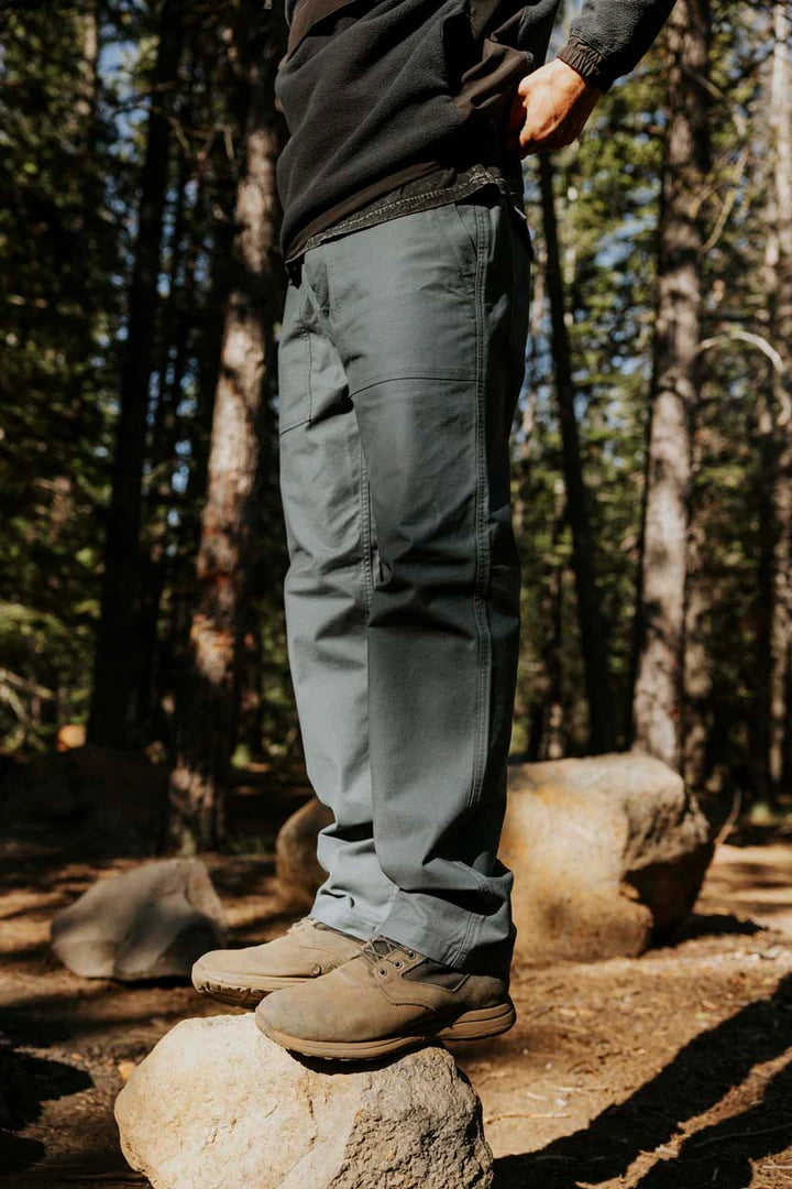 A man standing on a rock in the woods while wearing the Layover Utility Pants by Roark