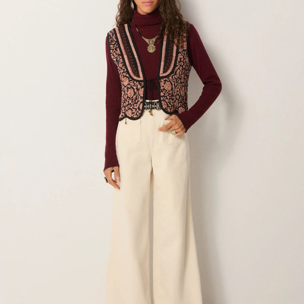 
                      
                        Person wearing a burgundy sweater, patterned vest, and white pants from Maison Hotel
                      
                    